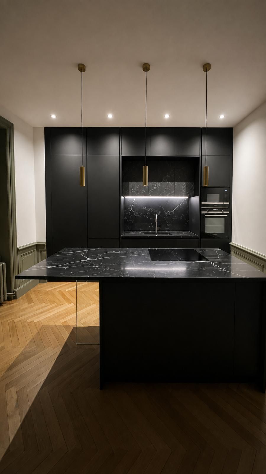 Cuisine noire avec îlot central en marbre noir veiné, plaque induction intégrée et suspensions laiton
