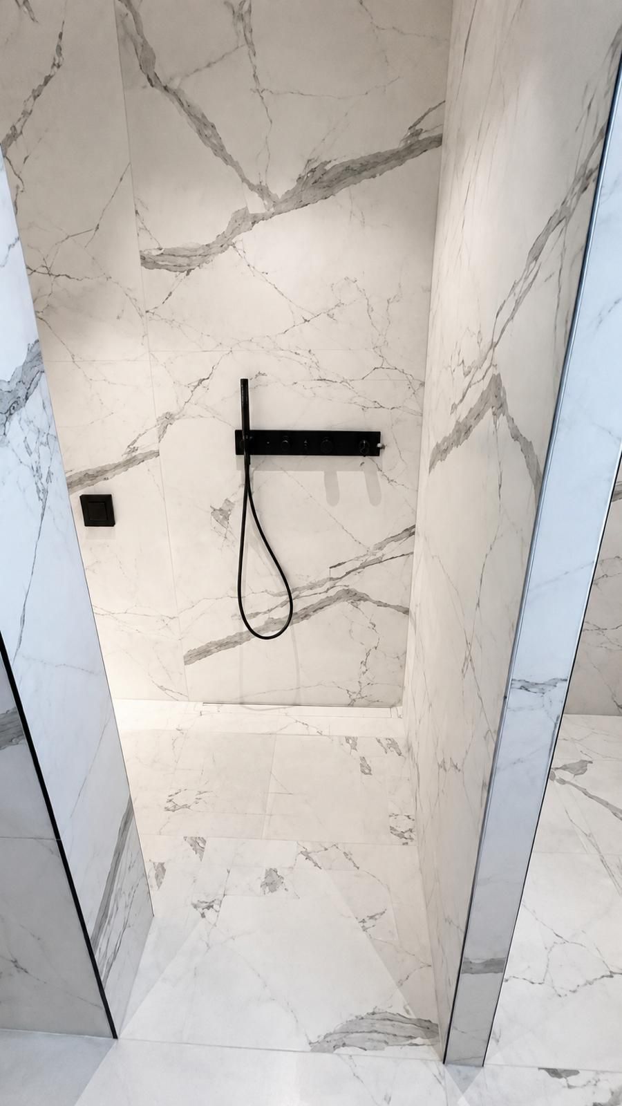 Douche à l’italienne carrelée en marbre blanc avec robinetterie thermostatique encastrée noire